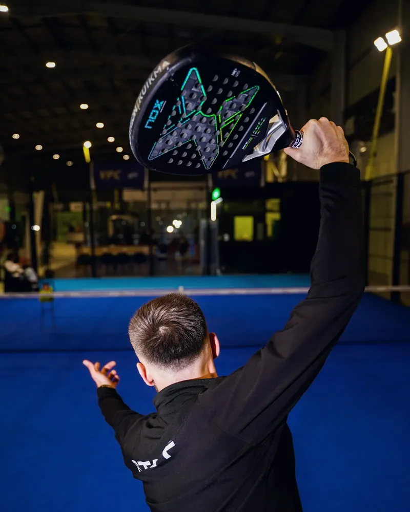 Padel player serving on an indoor court