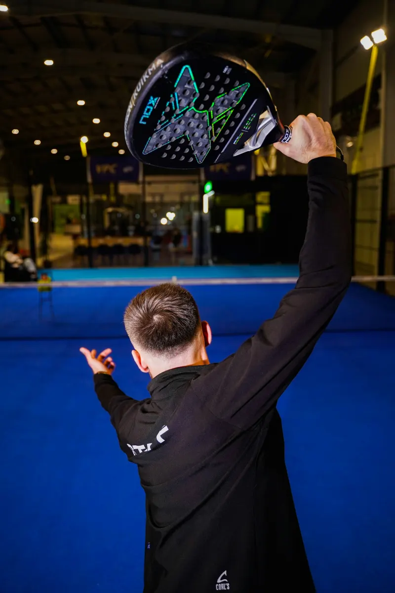Padel player lining up an overhead on an indoor blue court