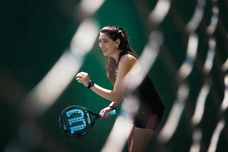 Smiling padel player ready at the back of the court, seen through the fence